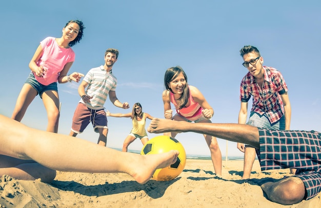Group of multiracial friends playing beach soccer at beginning of summer