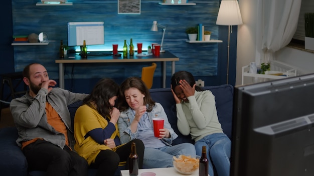 Group of multiracial people sitting comfortable on couch while watching thriller movie