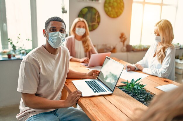 Group of multiracial people working in modern office during coronavirus. Young business people and senior boss are working together wearing face protective masks. Preventive measures during Covid-19