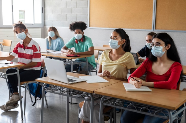 Group of multiracial teen highschool students wearing face mask listen to teacher lesson. Education concept. Healthcare concept.