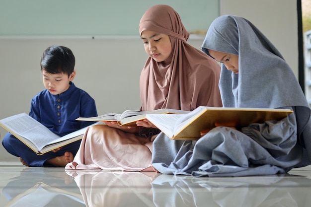 Group of muslim children sitting on the floor inside mosque and reading Quran together during Ramada