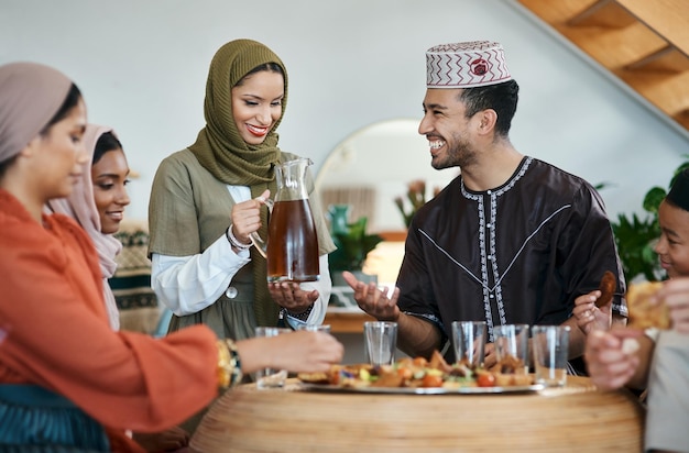 Group of muslim people celebrating Eid or Ramadan with iftar at home with food drink and family Young Islam woman pouring juice for a happy smiling and positive man while breaking fast together