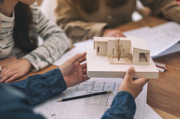 Фото Группа архитекторов, работающих и обсуждающих о модели архитектуры вместе с магазином чертежной бумаги на столе в офисе