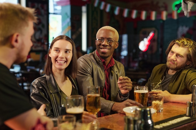 写真 テーブルに座ってビールを飲み、パブで休んでいる間互いに話している幸せな友人のグループ