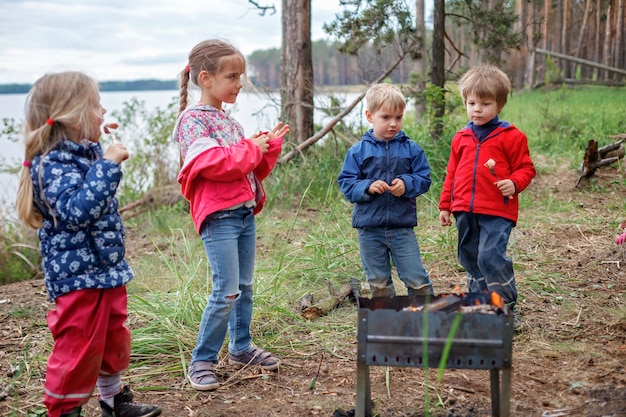 火のそばに座ってキャンプファイヤーでマシュマロキャンディーを焼く準備をしている子供たちのグループ、週末のハイキング、封鎖後の地元旅行、ステイケーション