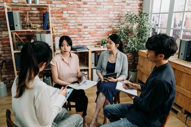 写真 会議室で密集して座っている人々のグループ。彼女が現代のオフィスでプロジェクトの意見を述べている間、女性の同僚を見ている女性と男性の労働者。チームワークの概念