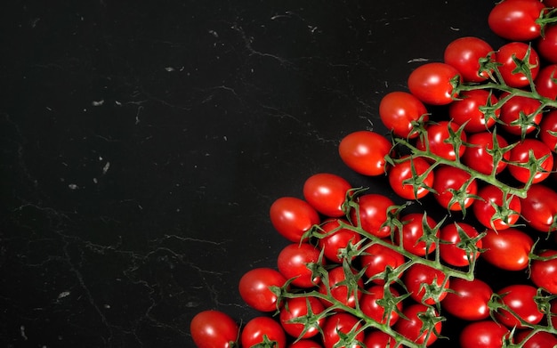 Фото Группа красных помидоров черри на черном мраморе, как доска, расположенная по диагонали - место для текста слева.