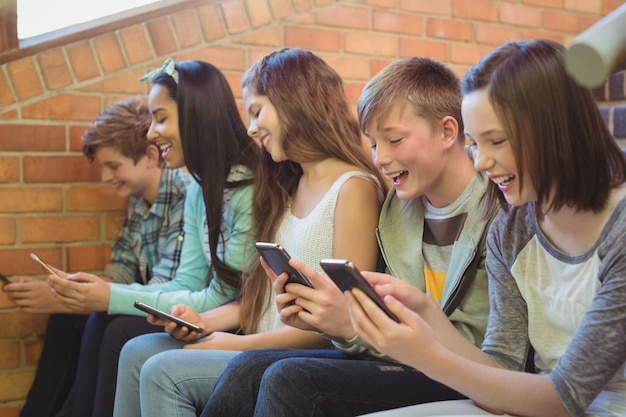 携帯電話を使用して階段に座っている笑顔の学校の友達のグループ