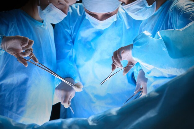 사진 파란색 톤의 수술실에서 일하는 외과의사 그룹. 수술을 수행하는 의료 팀