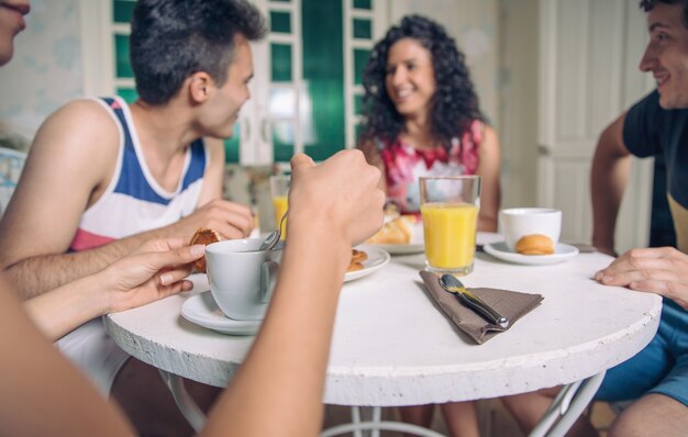 写真 家で一緒に笑って朝食を楽しんでいる若い友人のグループ。フォアグラウンドで一杯のコーヒーに焦点を当てます。