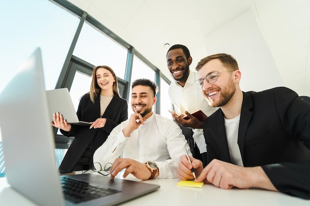 Group of office workers laughing while looking at laptop during meeting in office