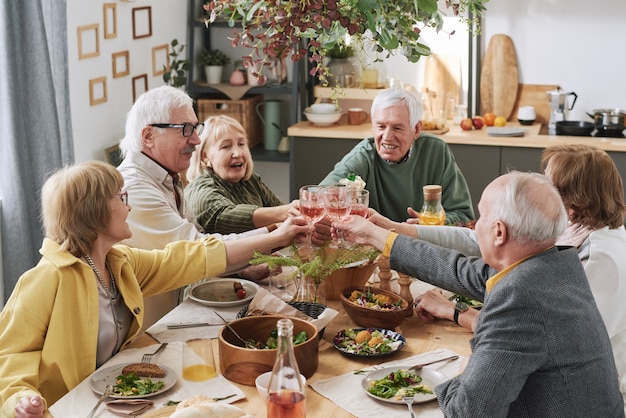 Group of old friends toasting with glasses of red wine while sitting at the table during dinner at home