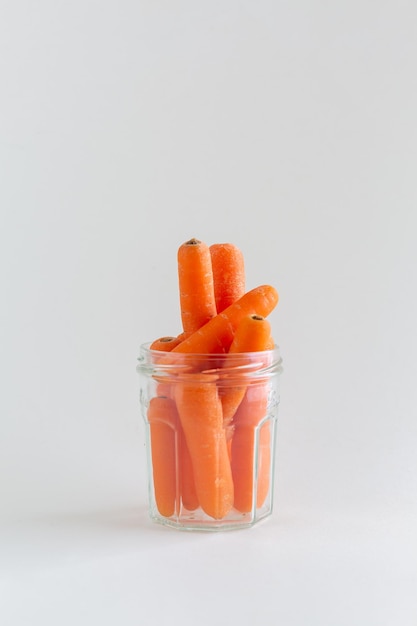 Группа апельсиновых моркови в стеклянной банки на белом фоне с копировальным пространством веганской закуски