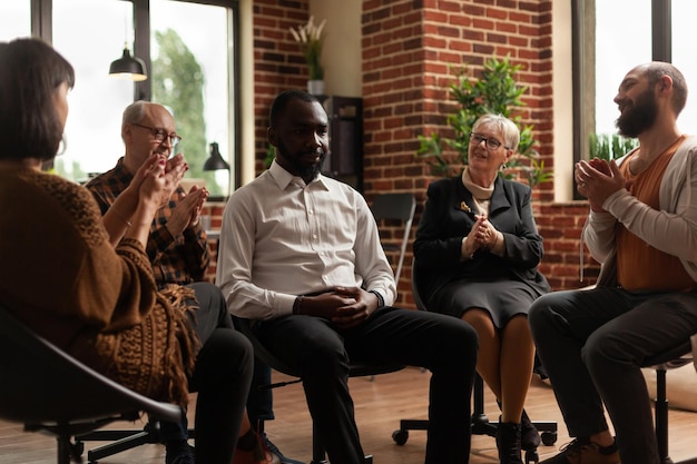 Group of people at aa meeting applauding success of man\
celebrating addiction achievement. patients at group therapy\
session clapping hands and sitting in circle, talking about\
progress.