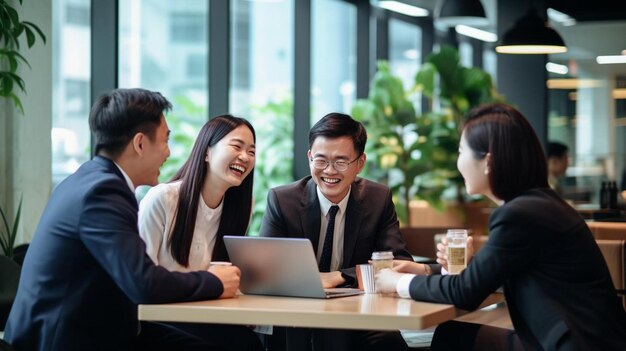 a group of people are sitting around a table with a laptop and a man in a suit is smiling and laughing