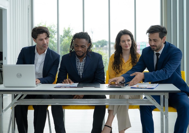 A group of people are sitting around a table with a laptop and papers They are all dressed