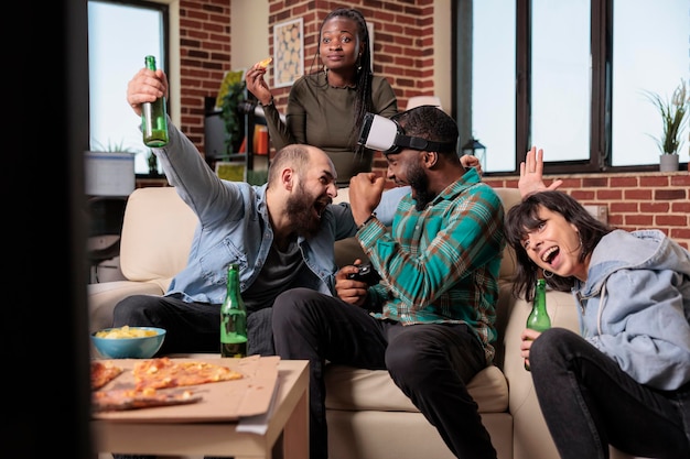 Группа людей празднует победу в видеоиграх на телевизионной приставке, играет в очки виртуальной реальности, чтобы выиграть. Счастливые друзья наслаждаются веселой деятельностью, собираются на домашней вечеринке.