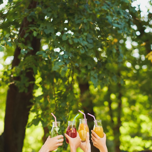 Group of people do cheers with detox juice cocktails on green nature