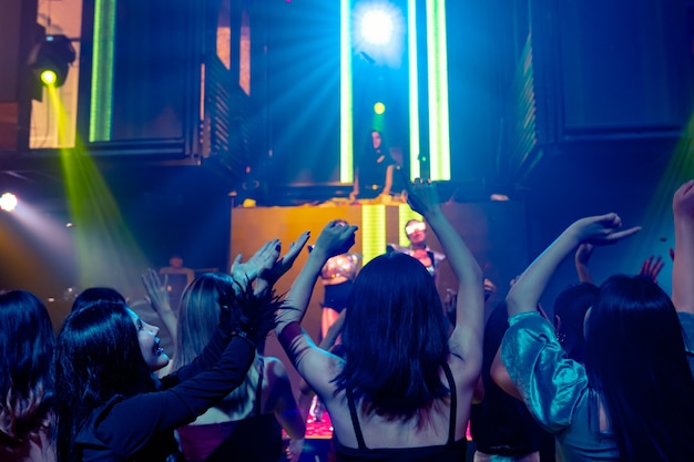 Group of people dance in disco night club to the beat of music from DJ on stage