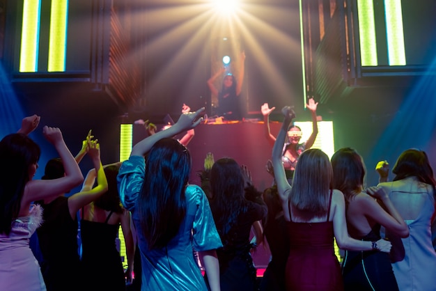 Group of people dance in disco night club to the beat of music from DJ on stage