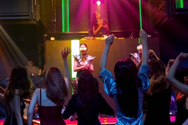 Group of people dance in disco night club to the beat of music from DJ on stage