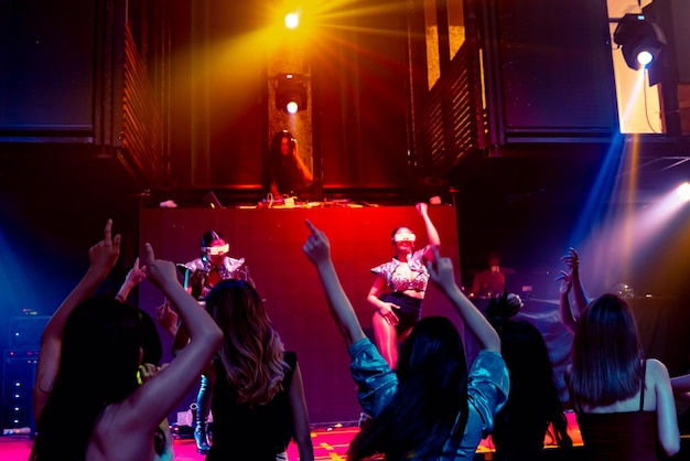 group of people dance in disco night club to the beat of music from dj on stage