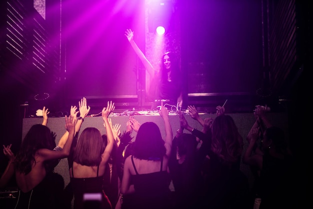 Group of people dance in disco night club to the beat of music
from dj on stage