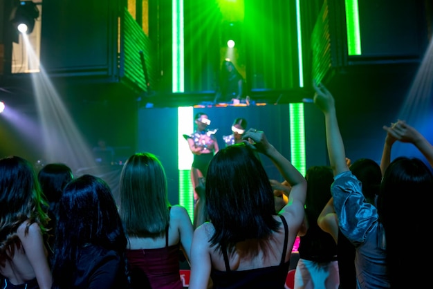 Group of people dance in disco night club to the beat of music from DJ on stage