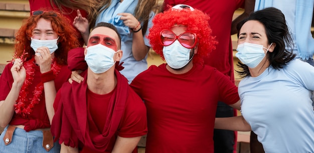 Gruppo di persone di razze diverse che rallegrano la loro squadra allo stadio di calcio con maschere facciali