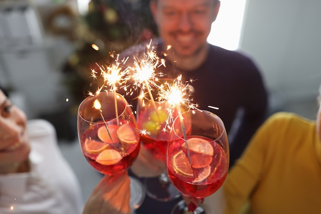 Group of people drinking cocktails from glasses with sparklers in front of christmas tree closeup