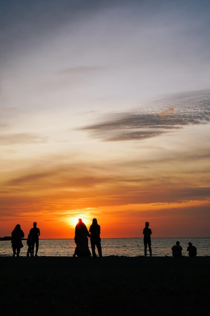 ビーチで夕日を楽しむ人々 のグループ。夕日の背景と人々 のシルエット