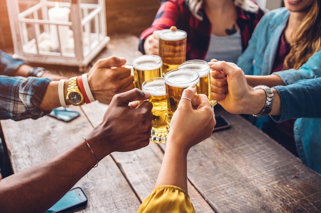 Group of people enjoying and toasting a beer in brewery pub - Friendship concept with young people having fun together