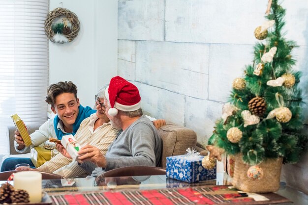 祖父と若い孫が家でクリスマスの夜を祝い、贈り物やプレゼントを渡す人々のグループ