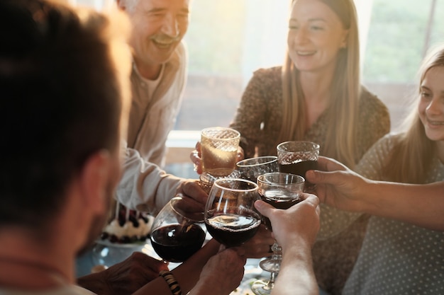 Group of people holding glasses with red wine and toasting they having fun at party