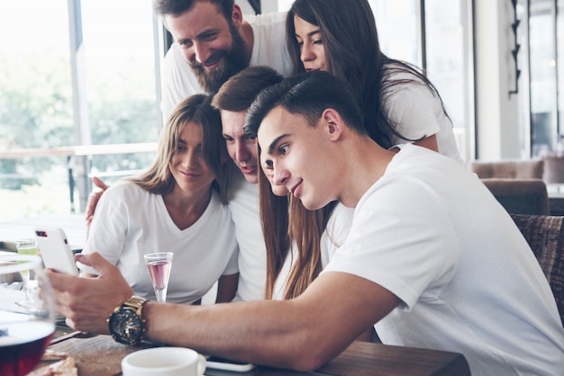 Un gruppo di persone fa una foto selfie in un caffè. i migliori amici si sono riuniti a tavola per mangiare la pizza e cantare vari drink