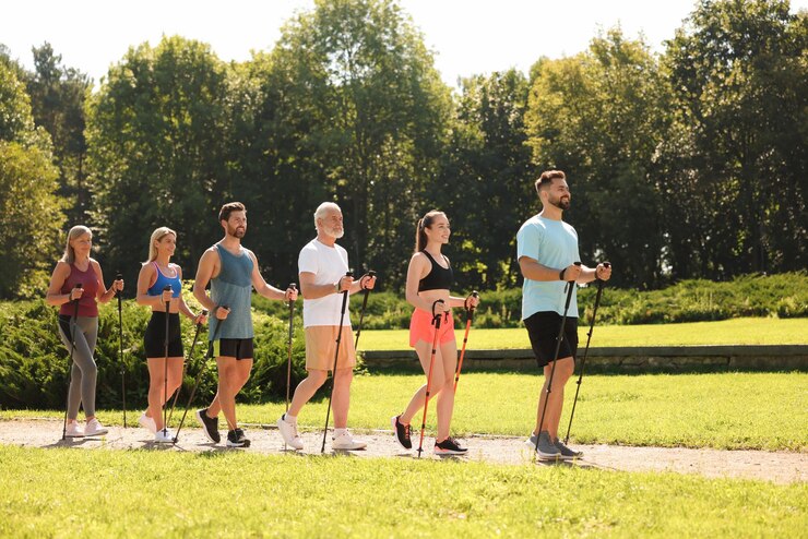 Photo group of people practicing nordic walking with poles in park on sunny day