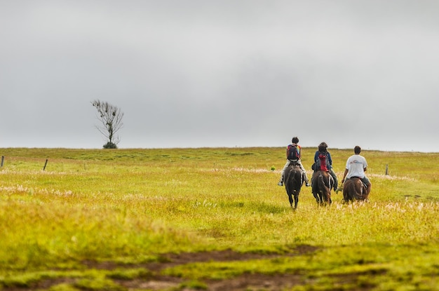 Group of people riding horses towards a flat hill at Easter Island Chile
