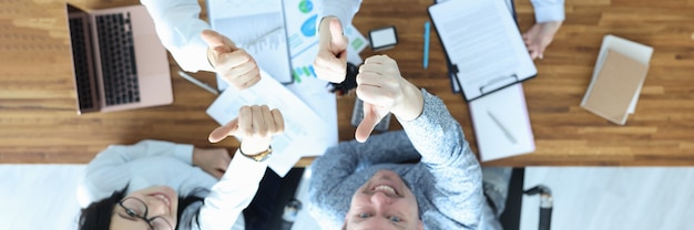 Il gruppo di persone che mostrano pollice in su al piano del tavolo visualizza il concetto di lavoro di partnership di successo