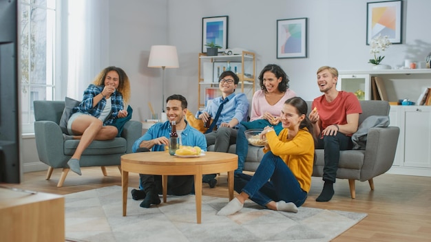 A group of people sit on a couch and watch a tv show.