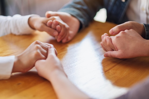 Gruppo di persone sedute in cerchio che si tengono per mano e pregano insieme o in una sessione di terapia