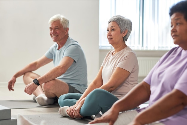 Group of people sitting on exercise mats and exercising together in yoga studio