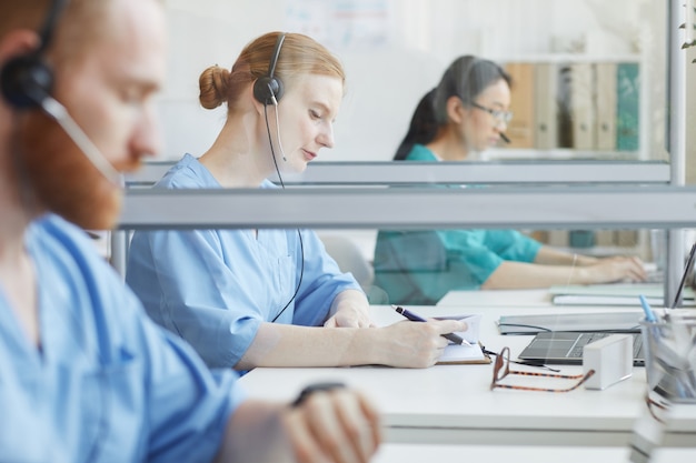 Group of people sitting at the table and talking to clients in medical call center