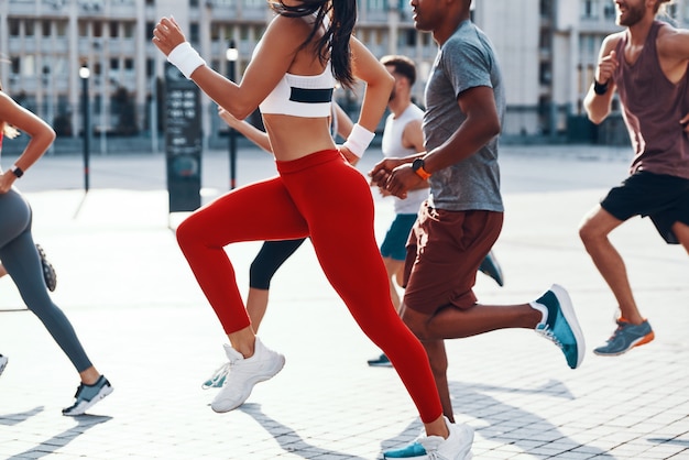 Gruppo di persone in abbigliamento sportivo che fanno jogging mentre si esercitano sul marciapiede all'aperto