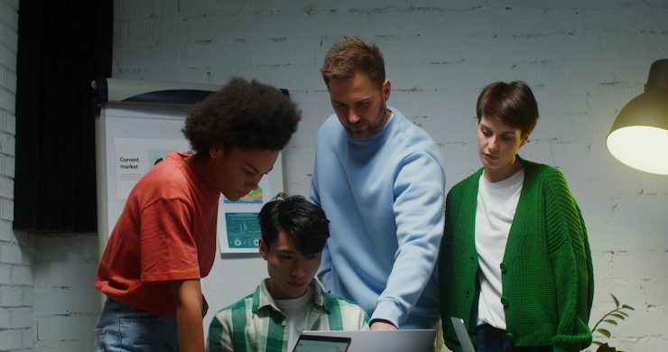 Photo a group of people stand near workplace of their colleague and look at his laptop