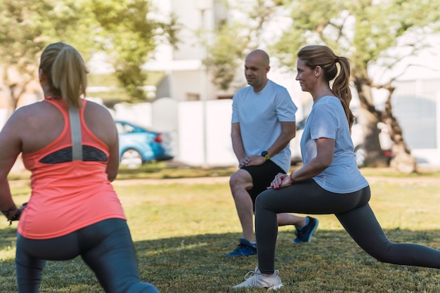 Photo group of people stretching while doing front splits in a park