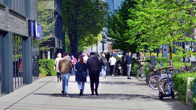 Группа людей идет по тротуару, один из которых имеет велосипед.