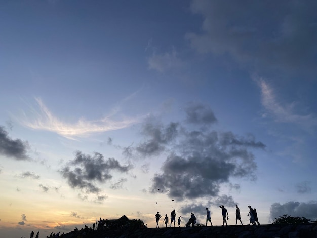 A group of people walk on a hill with a sunset in the background.