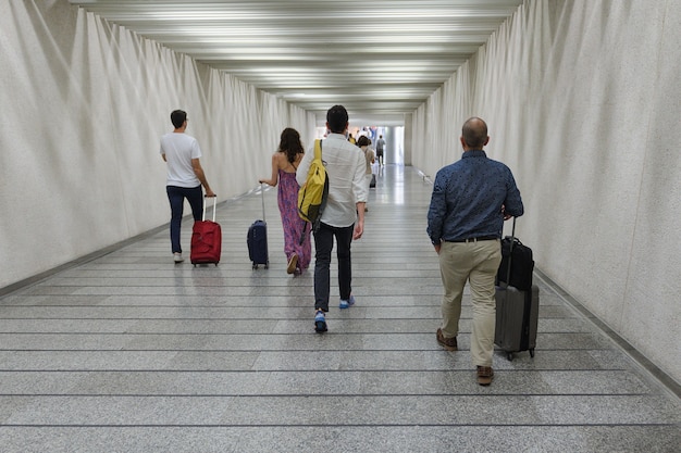 Photo group of people with suitcases on wheels go through the underpass rear view