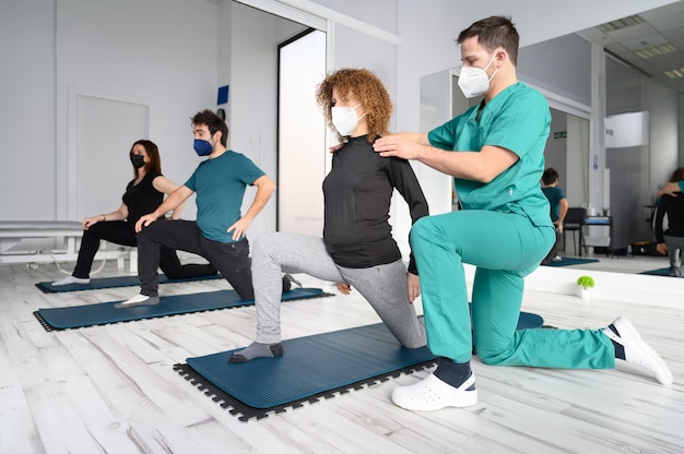Группа людей на ковриках для йоги, которым помогает физиотерапевт в реабилитационной клинике.