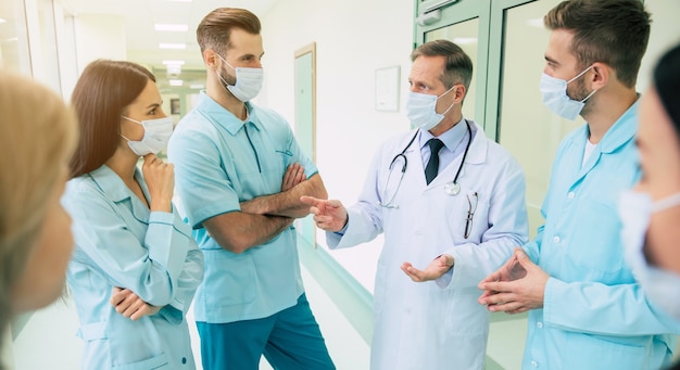 Group photo of young medics during a conversation with the senior confident doctor in the hospital corridor